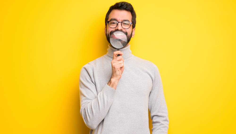 Homme qui tient une loupe au niveau de son sourire